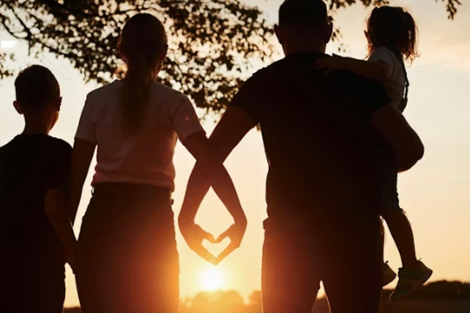 A family silhouette at sunset with parents forming a heart shape with their hands